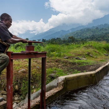 Man working on a device in water with cloud covered mountains in background
