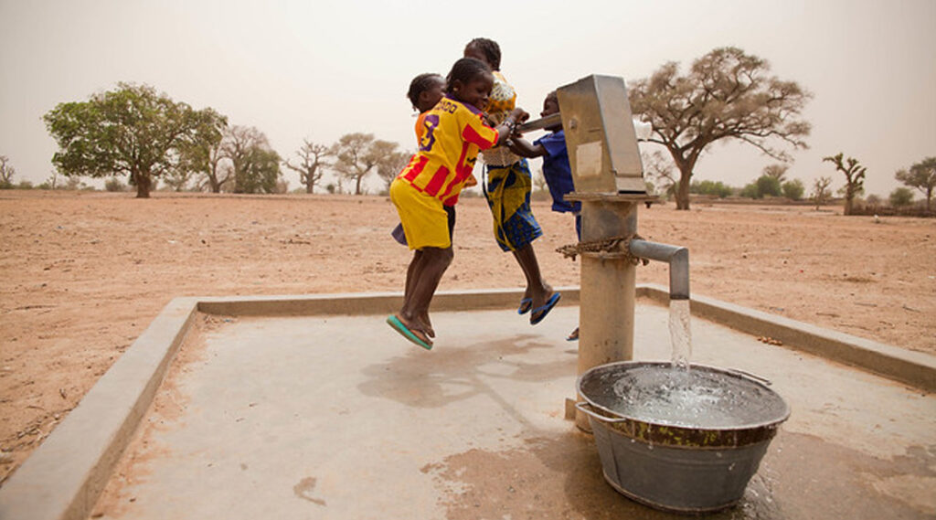four kids jumping to use a water pump