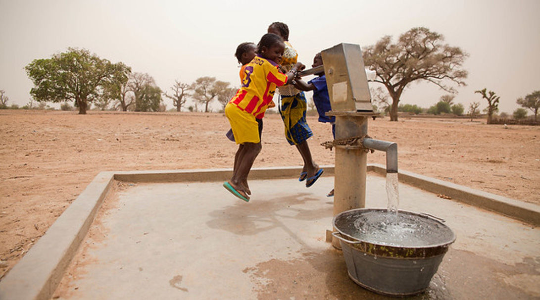 four kids jumping to use a water pump